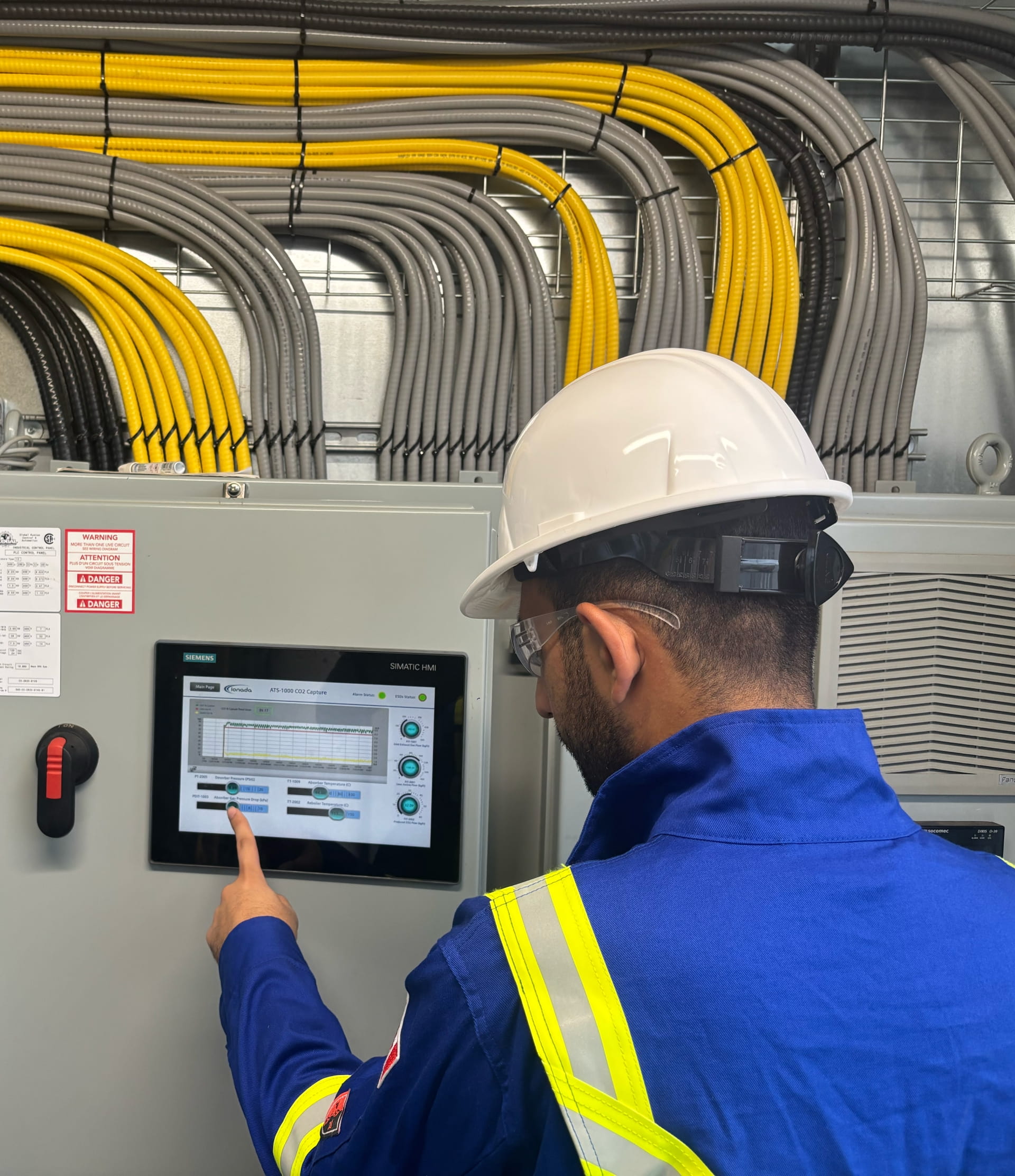 Engineer in protective gear operating an industrial control system, illustrating hands-on development, testing, and optimization of carbon capture technology for reducing emissions in industrial applications.