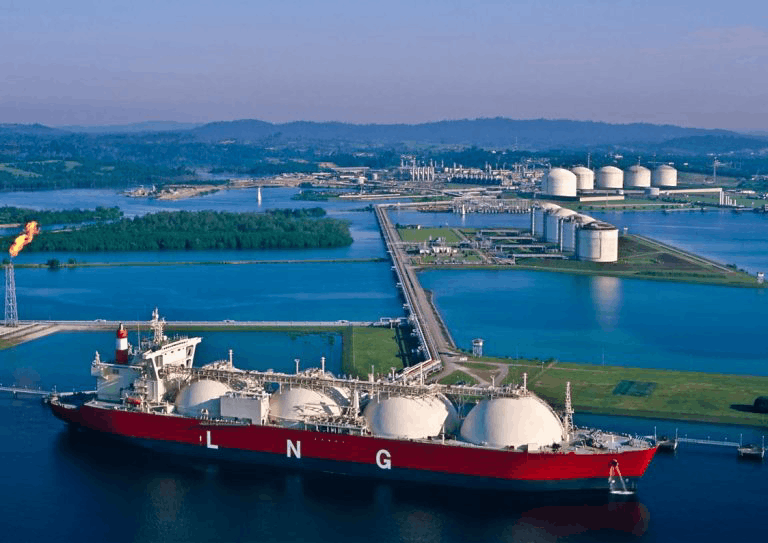 LNG carrier docked at a waterfront terminal with spherical storage tanks and surrounding industrial infrastructure, highlighting the role of emissions-reduction technologies in helping large marine vessels reduce harmful exhaust and support cleaner shipping operations.