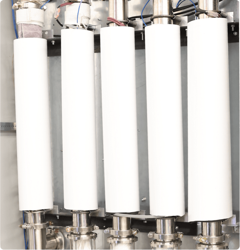 Close-up of cylindrical membrane modules connected to stainless steel piping, illustrating compact membrane-based carbon capture technology designed to separate CO₂ from industrial exhaust streams and help reduce emissions.